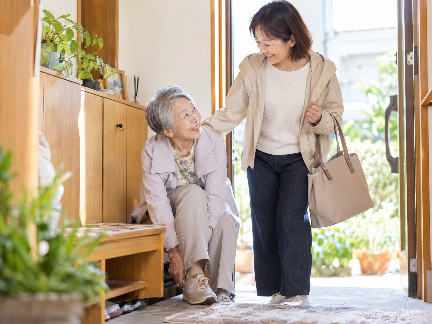 高齢女性が外出準備をしていて、40〜60代くらいの娘さんがそばで気遣っている写真。